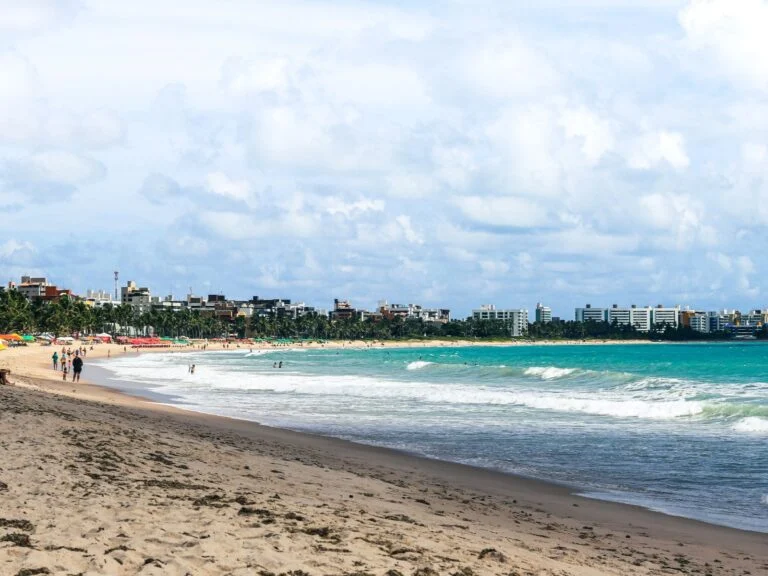 Praia da Paraíba com barracas e mar verde.